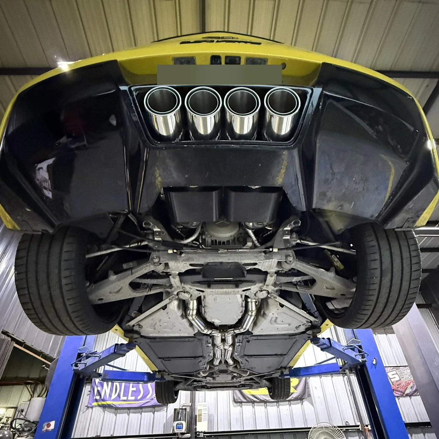Underside of a yellow Corvette C7 on the lift showing the X-pipe midpipes and quad polished Borla tips