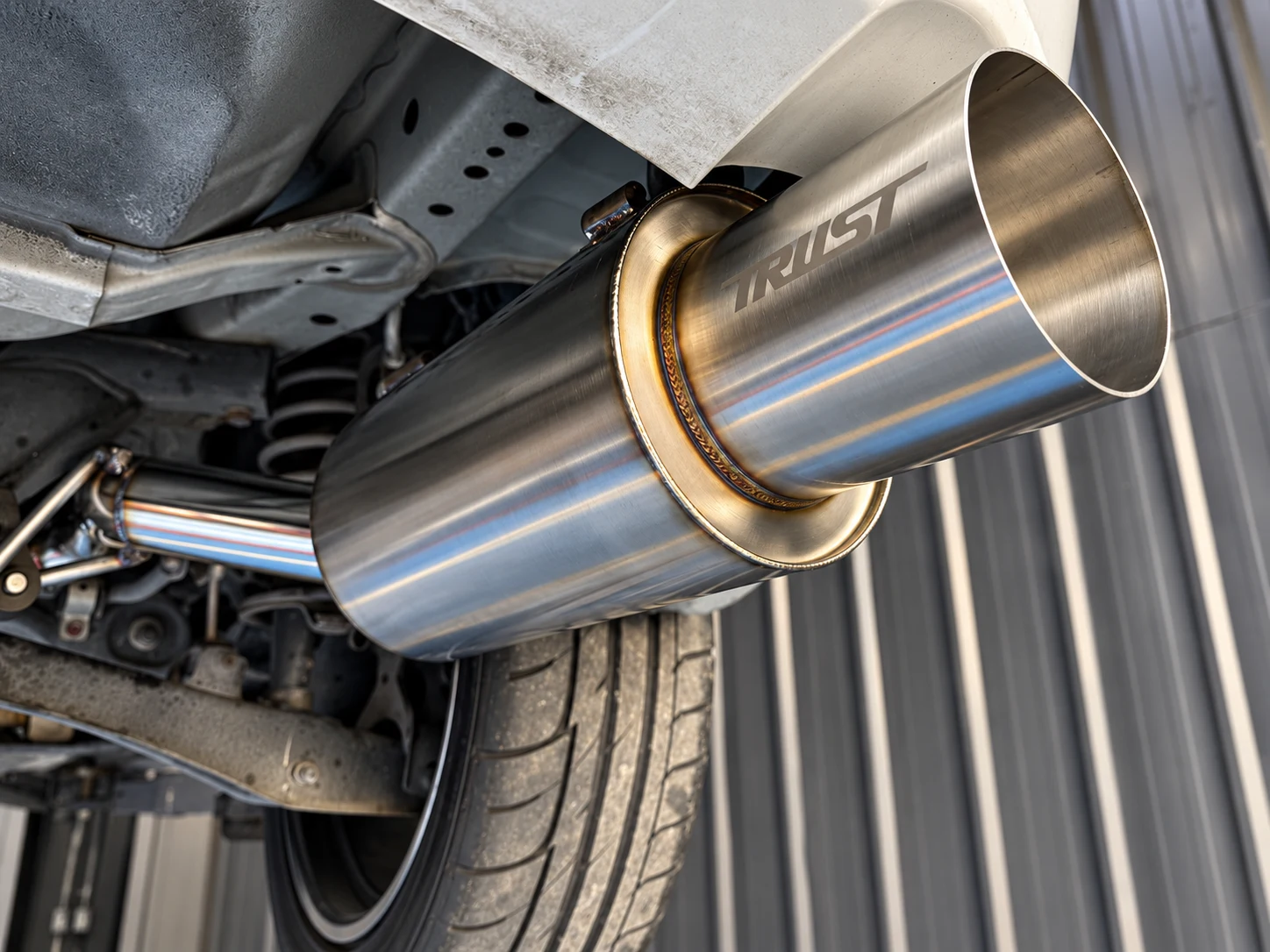 A stainless muffler with visible branding under a car